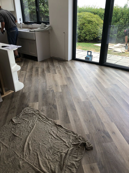 Dark wood effect vinyl flooring being installed.